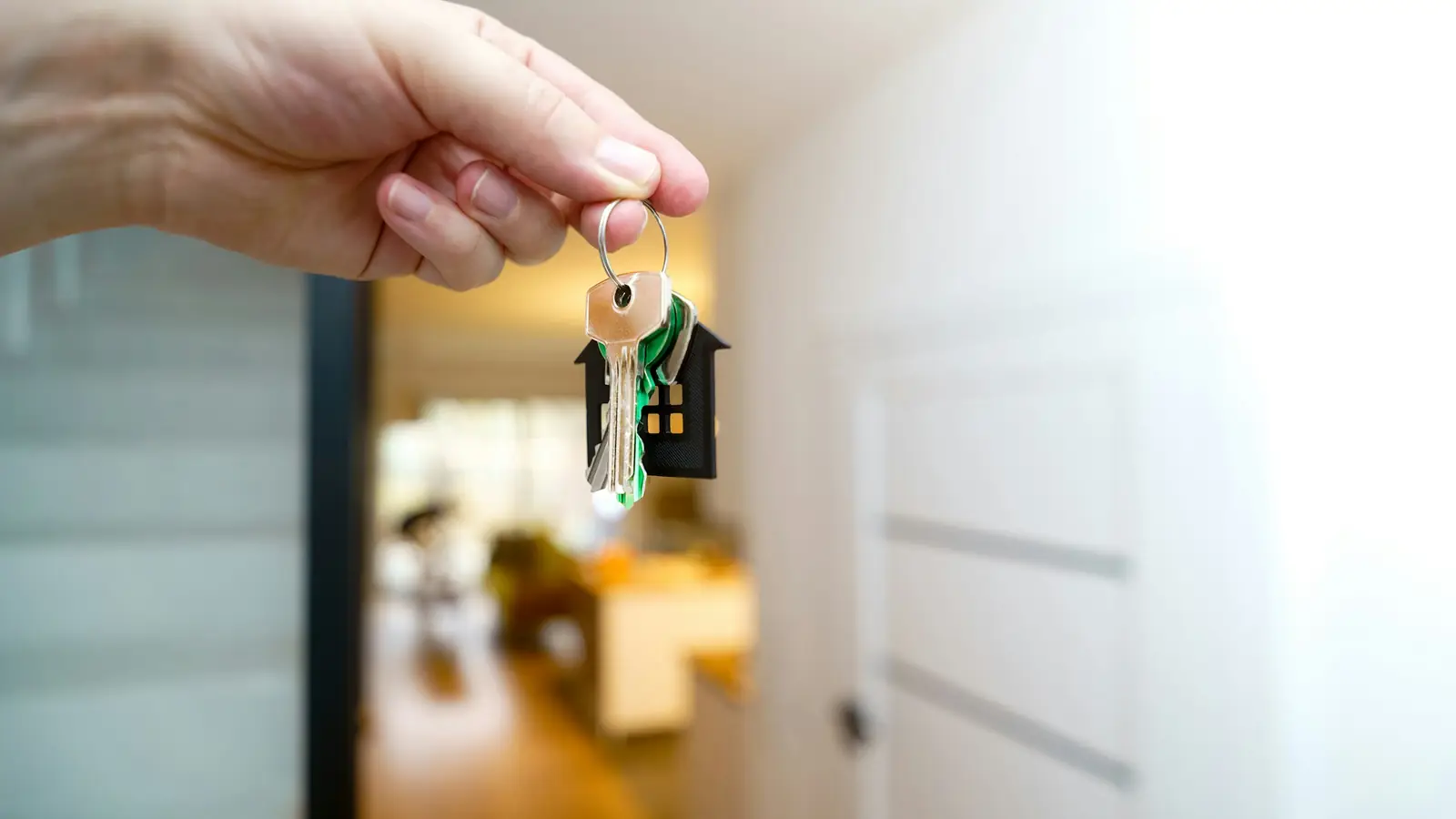 Hand met een sleutelbos en een huisvormige sleutelhanger in een woning